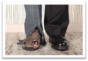 two legs standing together, one depicting a homeless man with worn out jeans and boots with holes, another in black business pants and shoes