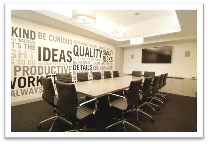 an empty boardroom/meeting room with a tv in the background and a large wall mural of words including 'ideas, quality, be curious, quality'
